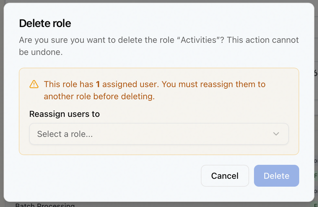 The Delete role dialog for a role that has members, showing the reassignment warning and the Reassign users to dropdown, with the Delete button disabled until a destination role is chosen